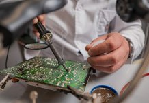Technik w białym fartuchu lutuje zieloną płytkę drukowaną